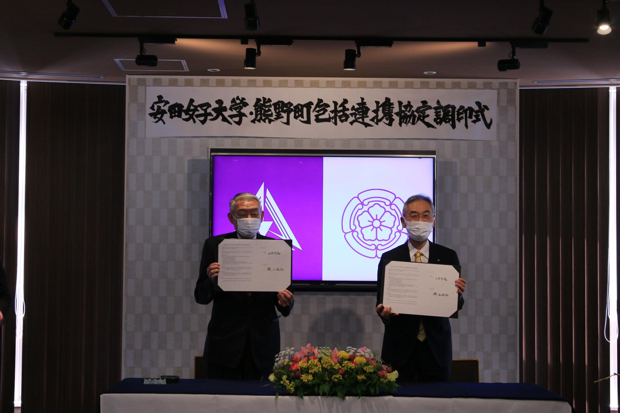 調印式で調印された書類を手に持ち写真にうつる二名の男性の写真