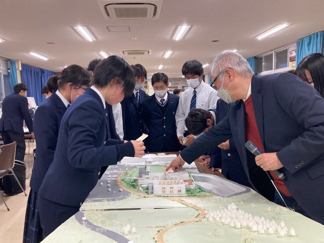 体験交流施設の模型を指さして意見交換を行う設計士と高校生たちの写真