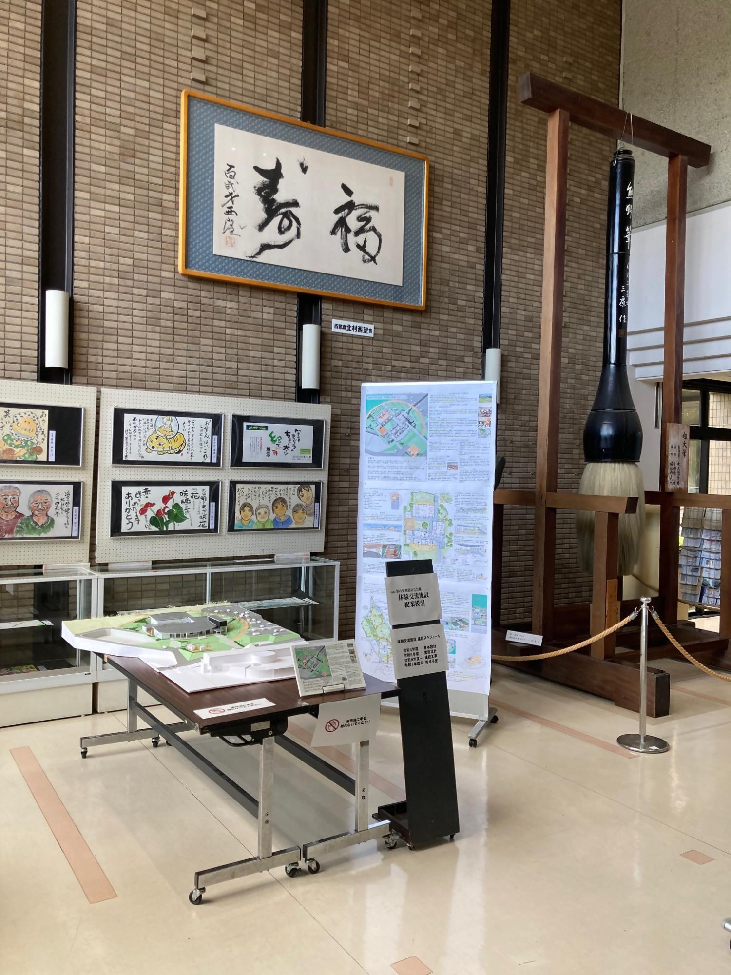 壁に掲示された書画や大筆、新体験交流施設の模型などがある町民会館のロビーの写真