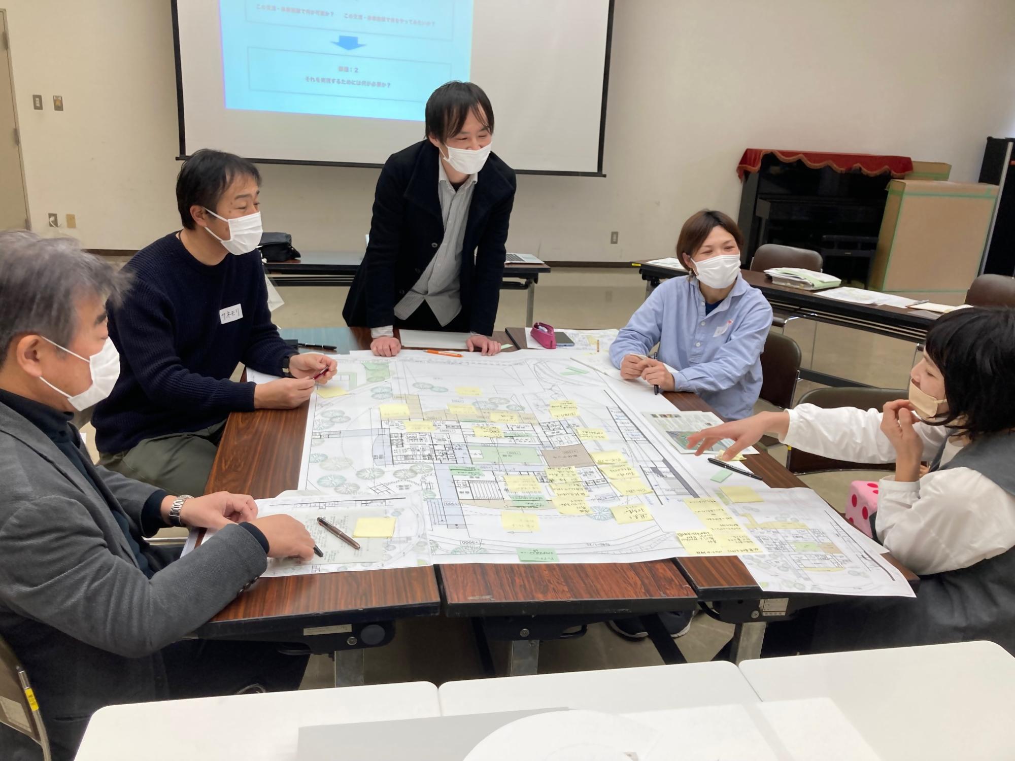 テーブルに広げた図面について話し合う町民の方々の写真