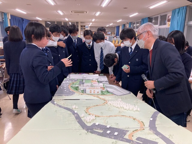 テーブルの上に広げられた町のジオラマの説明を受ける熊野高校の高校生の写真