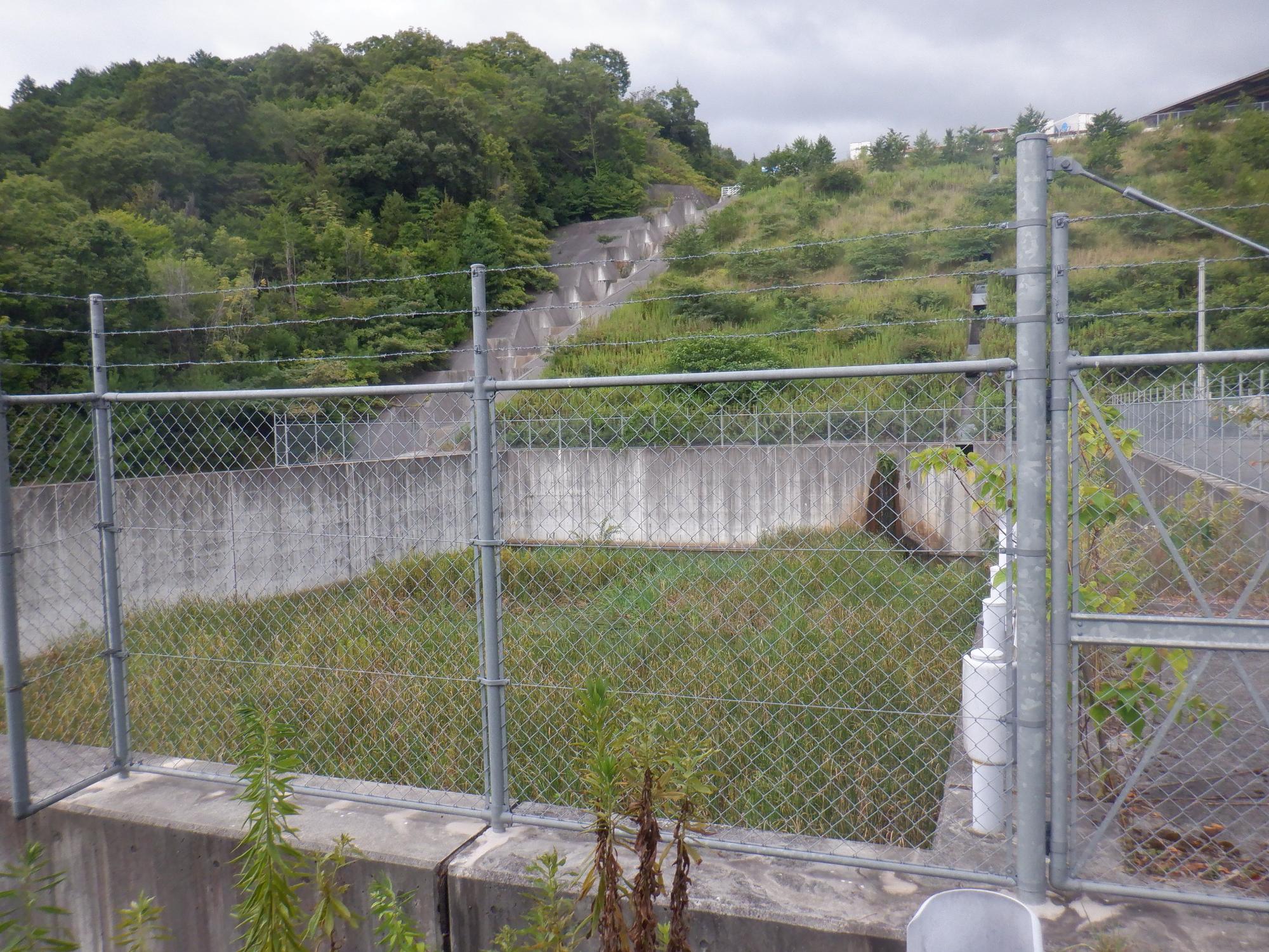 山間にあるフェンスに囲まれた調整池のイメージ写真