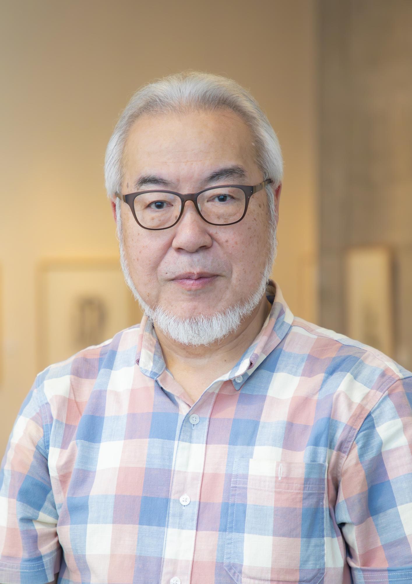 ピンクと水色のチェックのシャツを着た画家・野村重存さんの画像