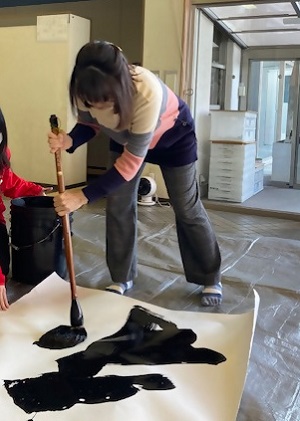 大きな紙に大筆で文字を書いている女性の写真