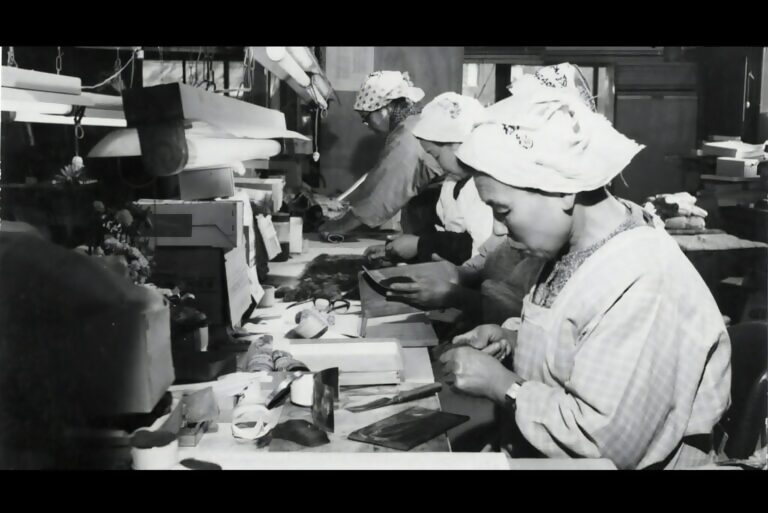 白い頭巾をかぶり着物を着た女性たちが器具を使って毛筆を作っている姿を捉えたモノクロ写真