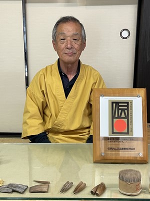 黄色い半纏を着ている熊野筆伝統工芸士会会長の男性の写真