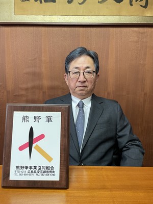 スーツを着て「熊野筆」と書かれた楯と共にうつる熊野筆事業協同組合理事長の男性の写真
