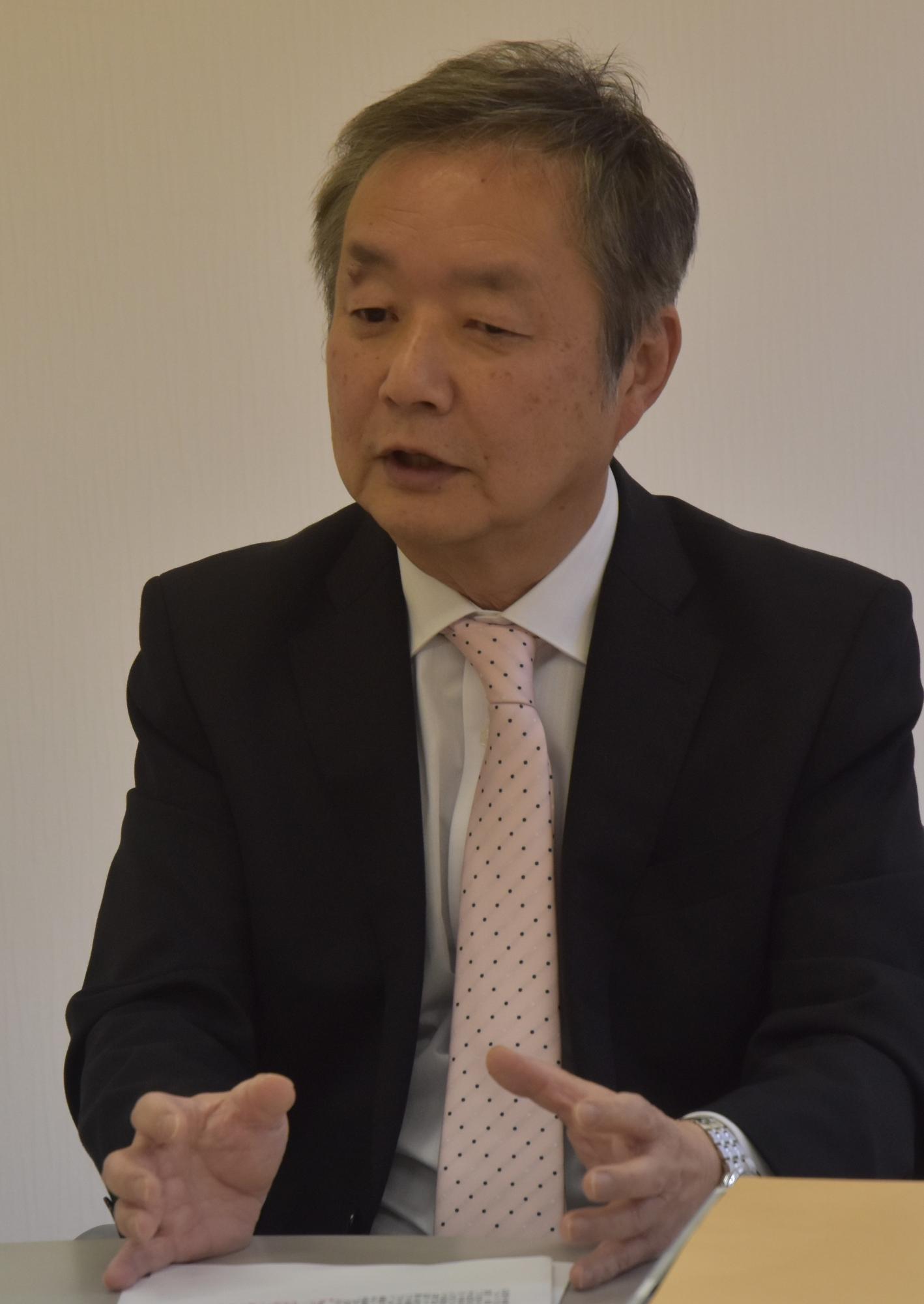 スーツ姿で質問に答える石井理事長の画像