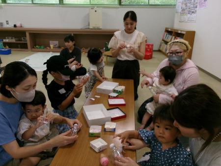 センター内の一室にある長テーブルに集まり、工作を楽しんでいる親子連れの写真