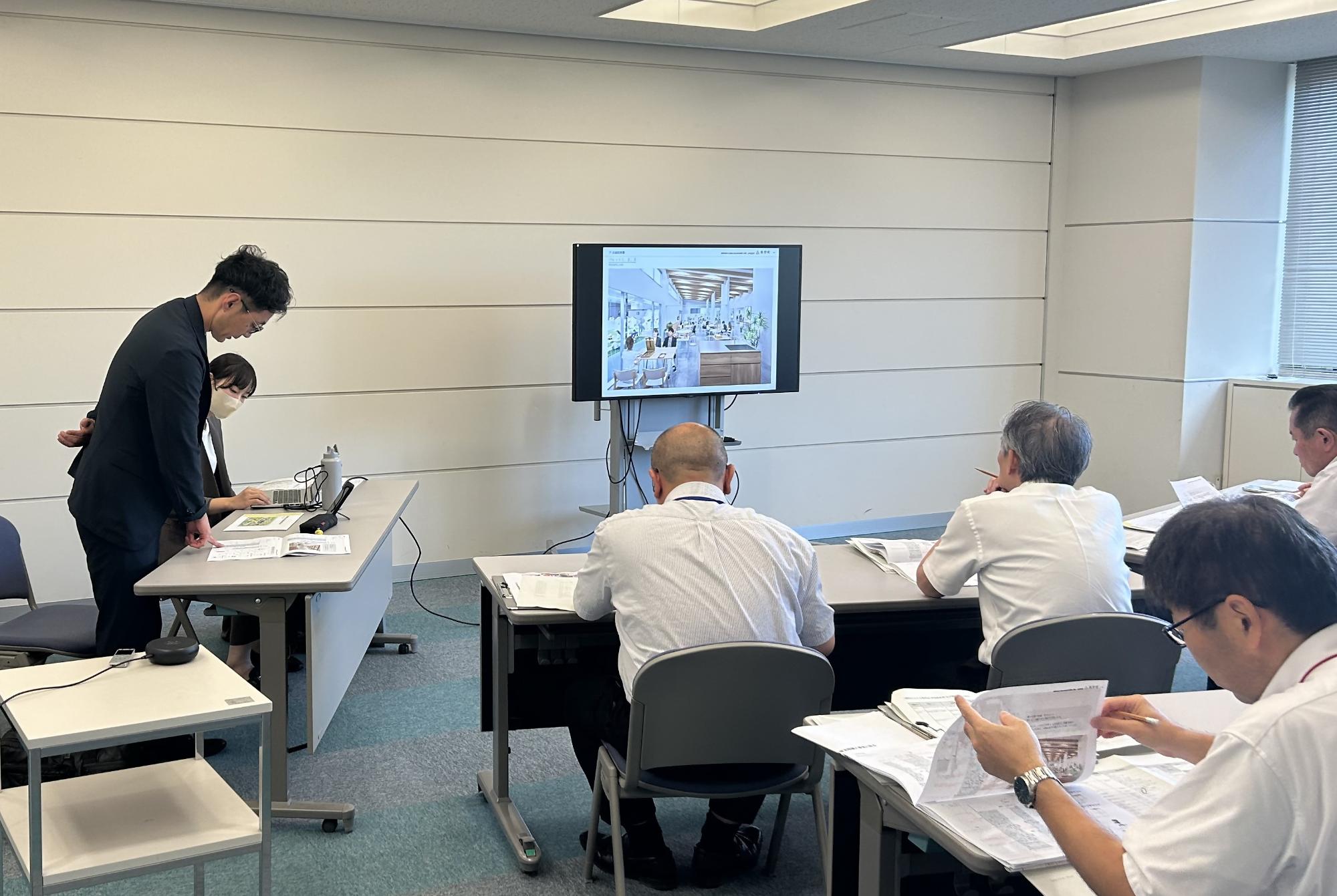 モニターを見ながら説明する男性のプレゼンテーション風景の写真